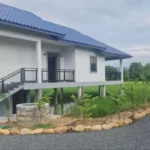 Exterior view of elevated white villa with blue roof, stone landscaping, and gravel driveway in Kampot countryside