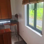 Mini bar area with wooden counter, bar stools and bamboo window shades overlooking garden