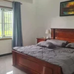 Master bedroom with traditional wooden bed frame, blue curtains, and Cambodian artwork featuring Angkor Wat at sunset