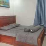 Master bedroom with wooden bed frame, bedside table, gray bedding and Cambodian landscape artwork